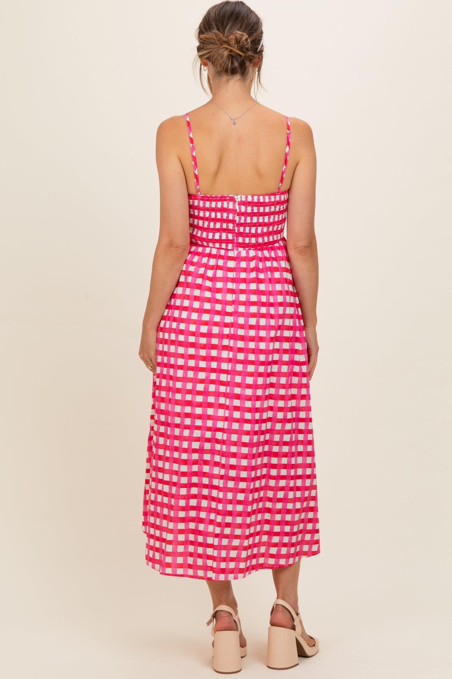 woman wearing a pink and white checkered maternity dress with a fitted bodice and flowing skirt, showing no baby bump