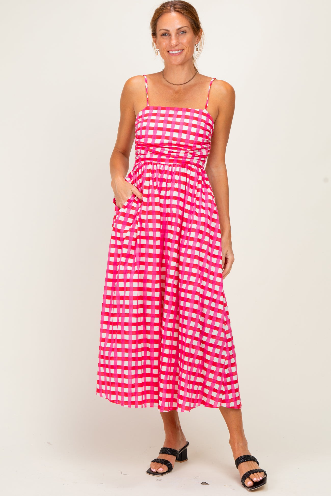 woman wearing a pink and white checkered midi dress with adjustable straps and pockets