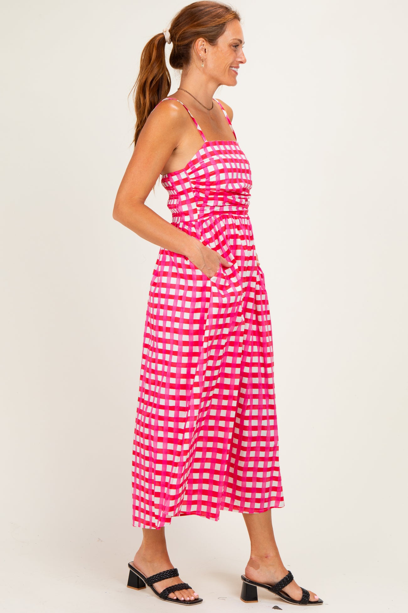 woman wearing a pink and white checkered midi dress with adjustable straps and side pockets