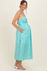 woman wearing a turquoise and white checkered maternity maxi dress with pockets and showing her baby bump