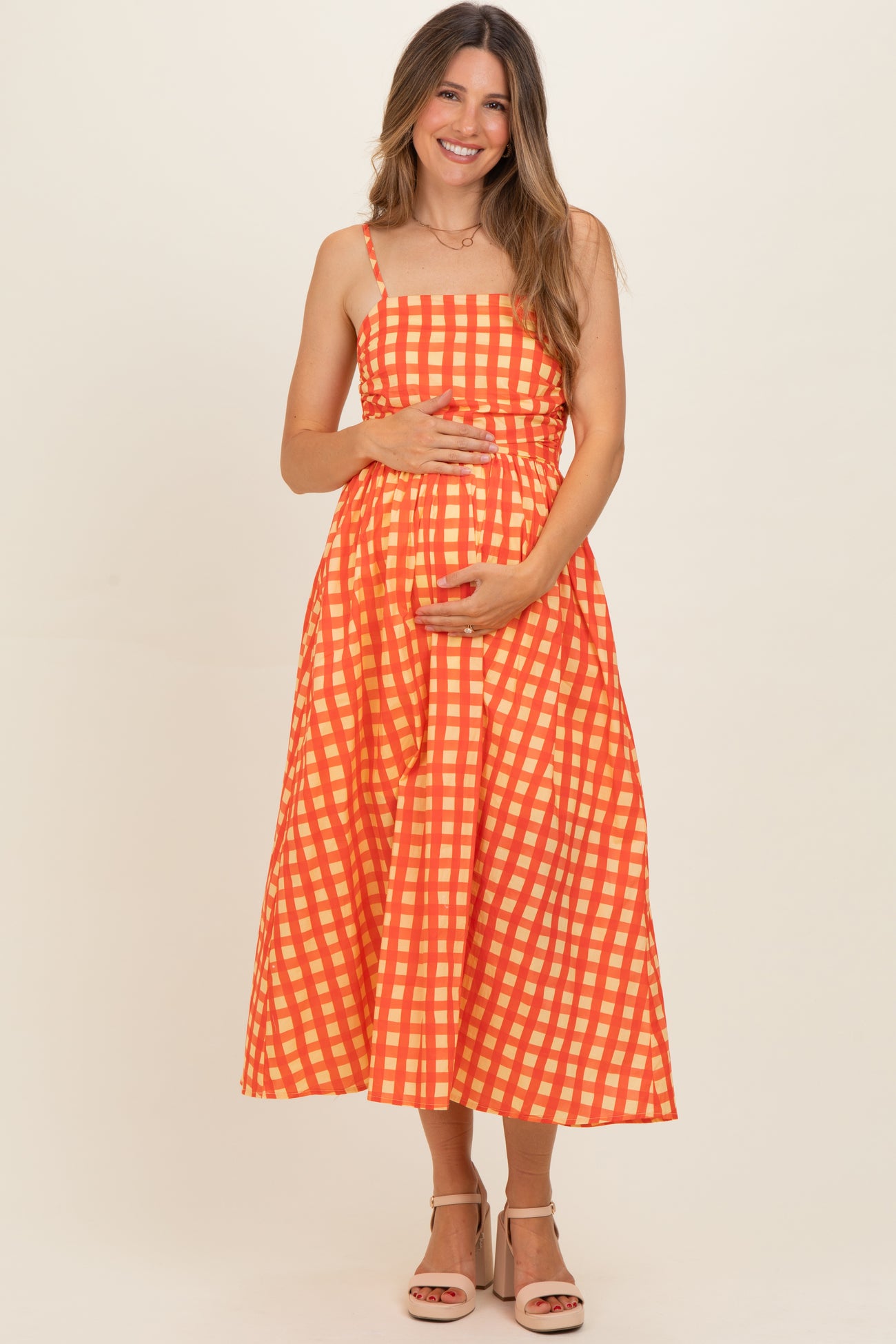 woman wearing a red and orange gingham maternity dress and holding her baby bump