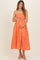 woman wearing a red and orange gingham maternity dress and holding her baby bump