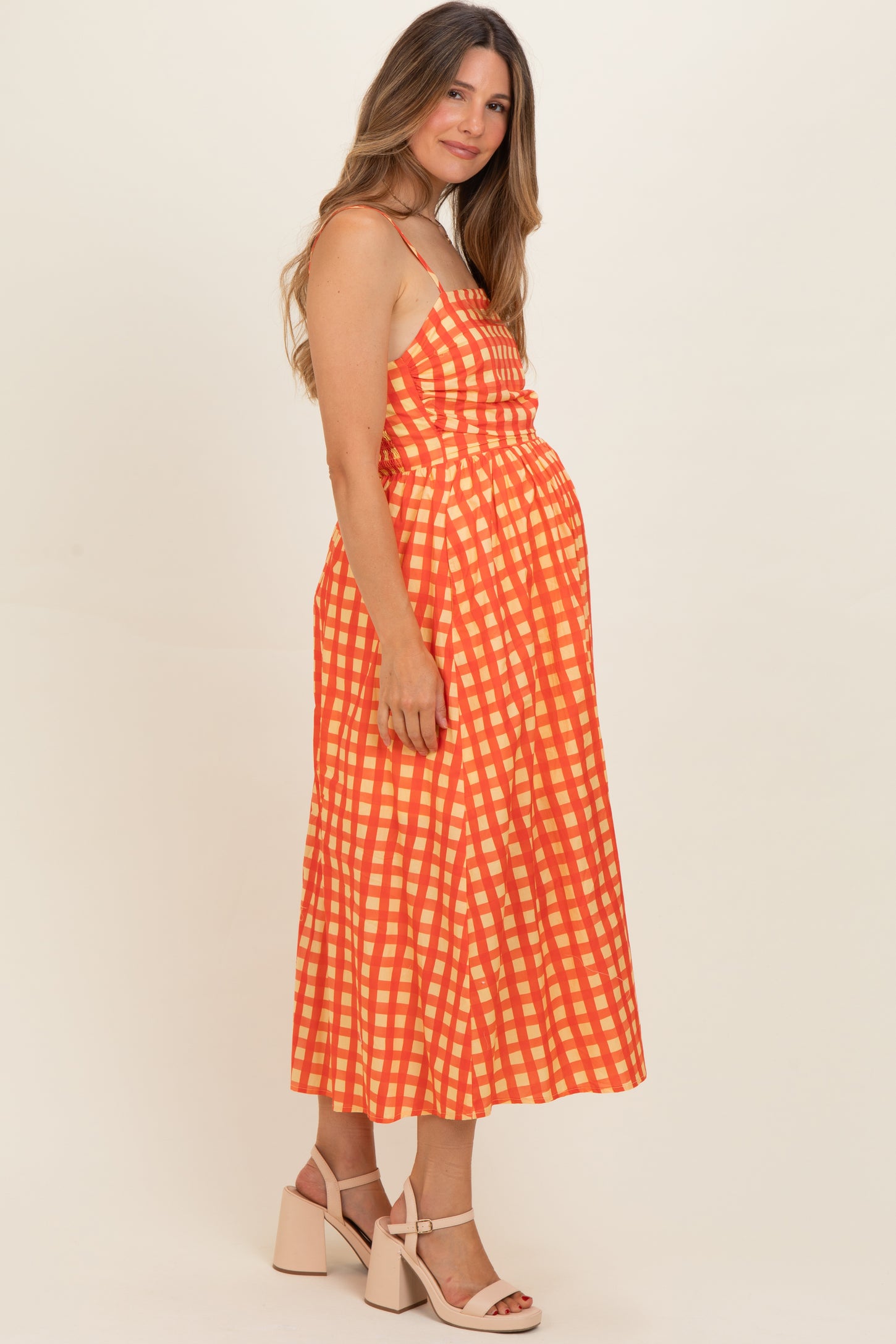 woman wearing a red and white checked maternity dress with spaghetti straps and a fitted waist, showing baby bump
