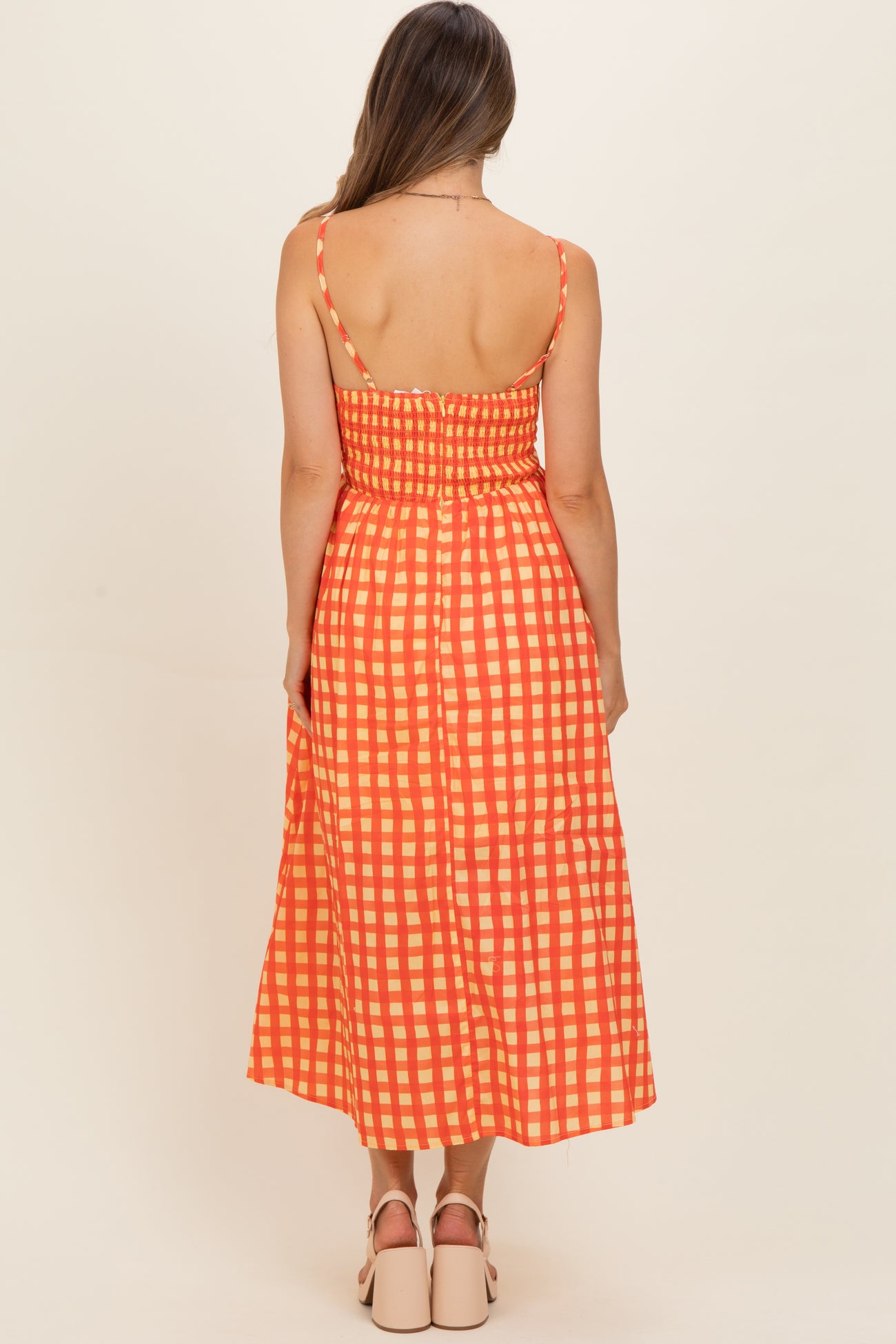 woman wearing an orange and cream checked maternity dress with a fitted bodice and flowing skirt from the back