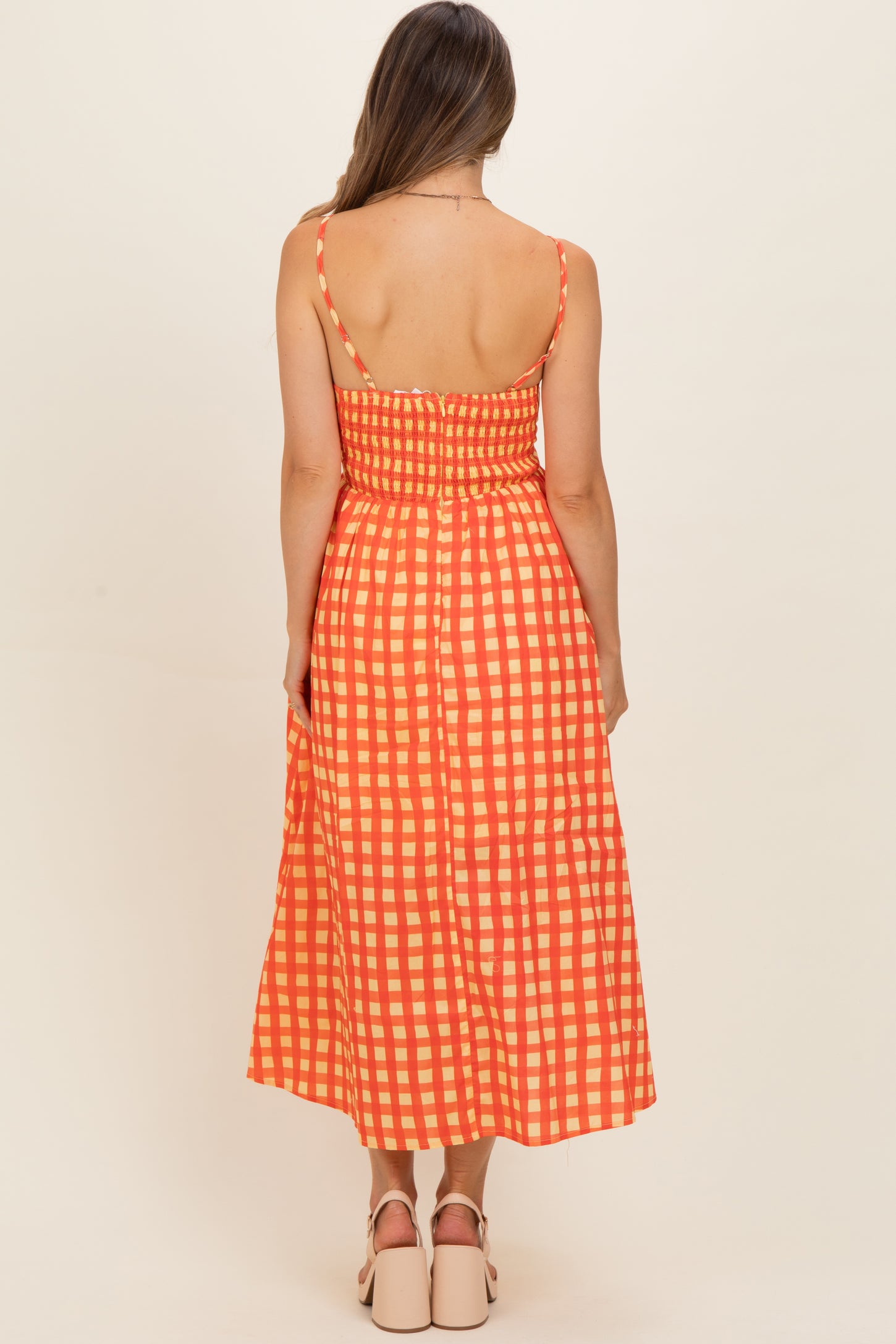 woman wearing an orange and cream checked maternity dress with a fitted bodice and flowing skirt from the back