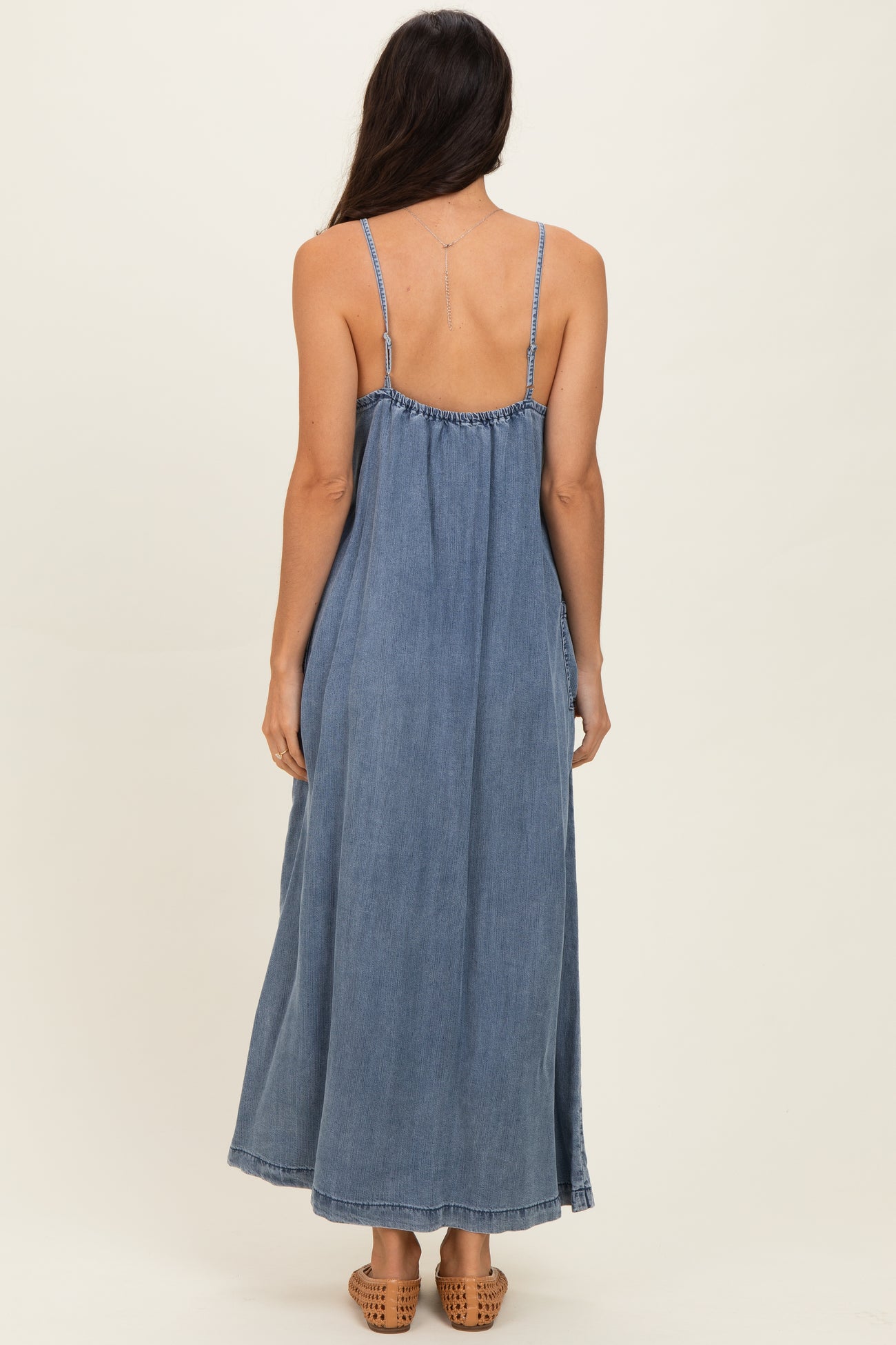 woman wearing a backless denim maxi dress with thin straps and a flowing silhouette