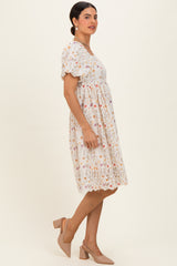 woman wearing a short sleeve white floral dress with a cinched waist and a flared skirt, paired with nude heels