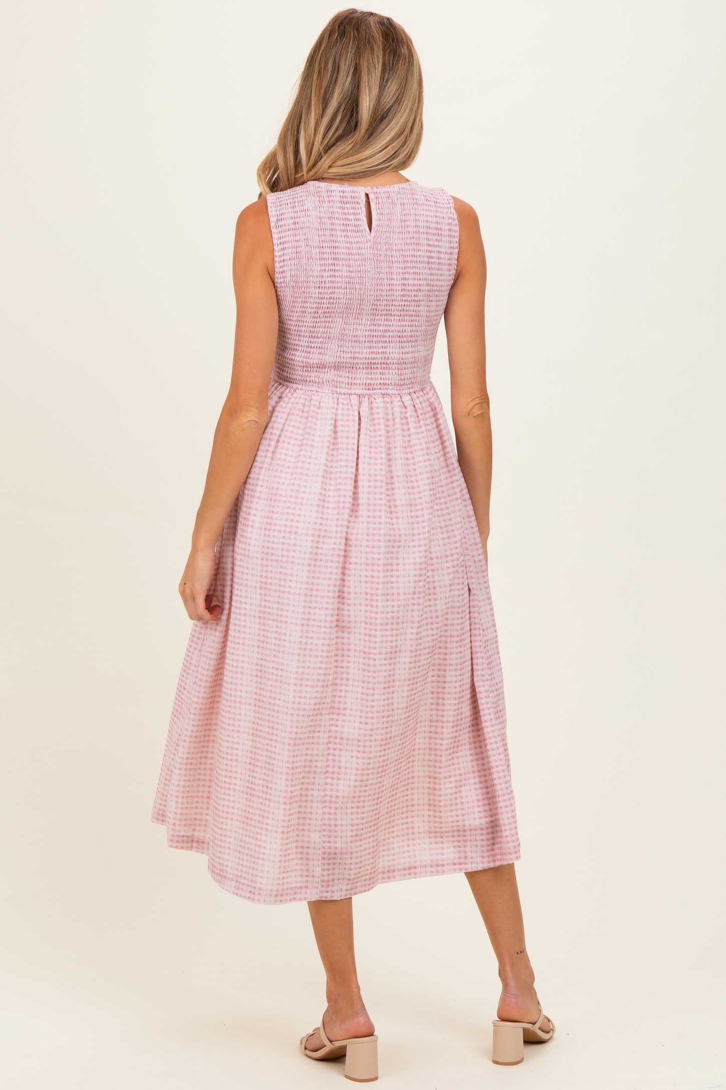 woman wearing a pink and white gingham maternity dress with a smocked bodice and a flowing skirt