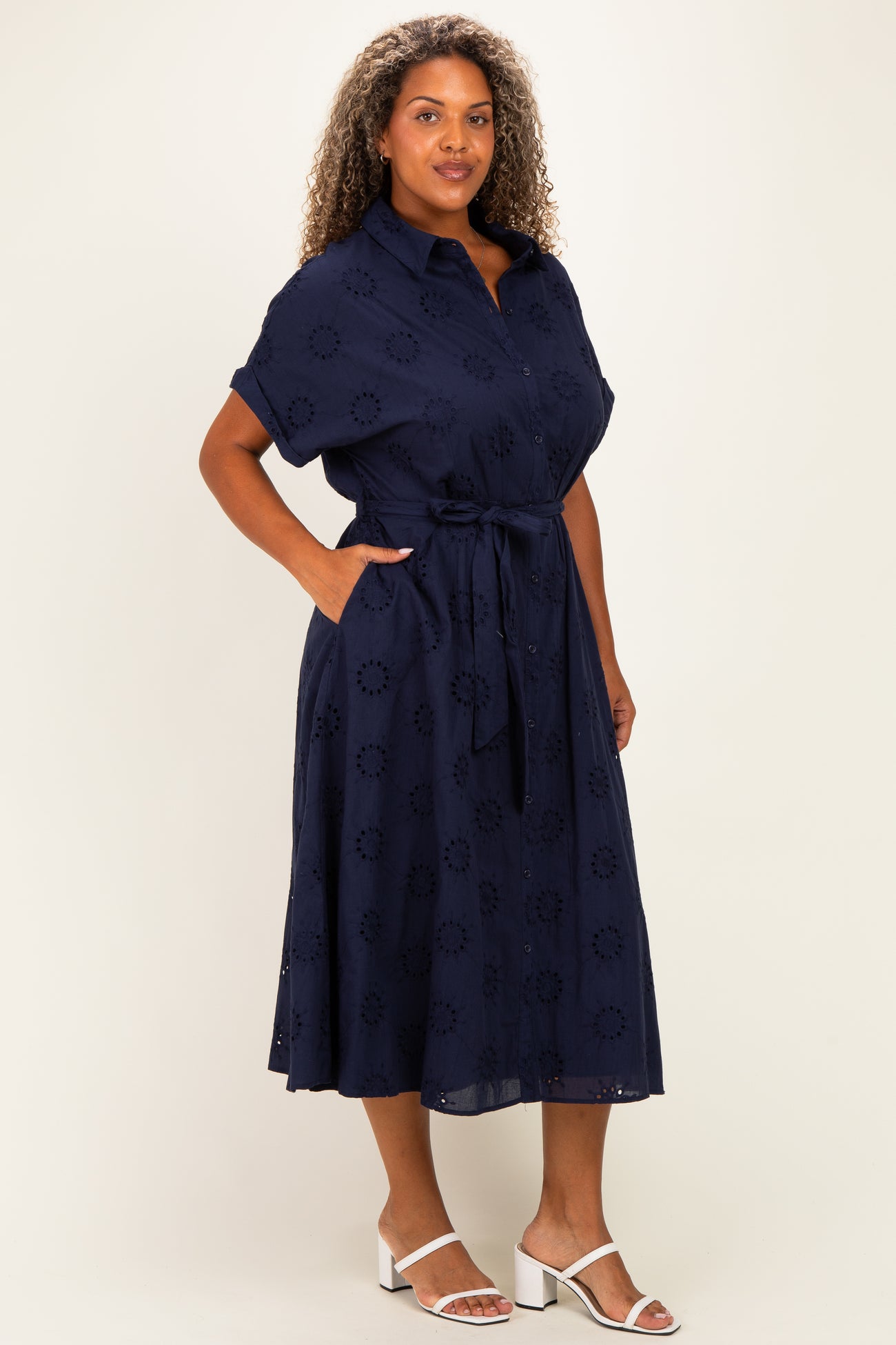 woman wearing a navy blue plus size dress with short sleeves, a tie belt, and floral embroidery details