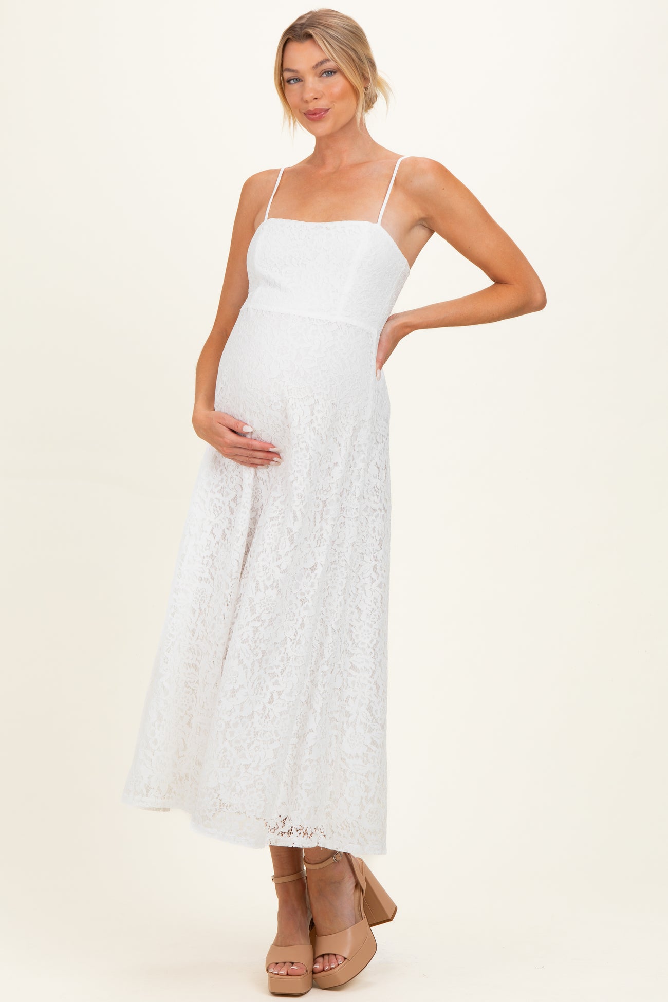 woman wearing a white lace maternity dress with spaghetti straps and holding her baby bump