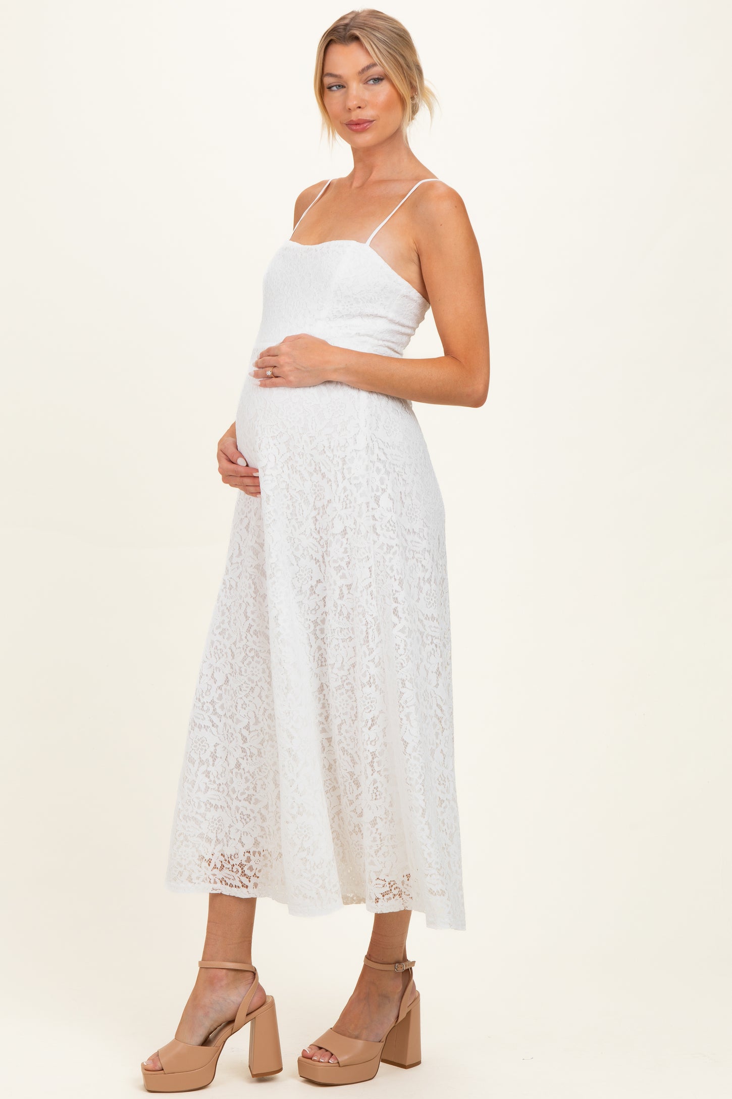 woman wearing a white lace maternity dress with spaghetti straps and holding her baby bump
