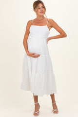 woman wearing a white maternity dress with tiered details and holding her baby bump