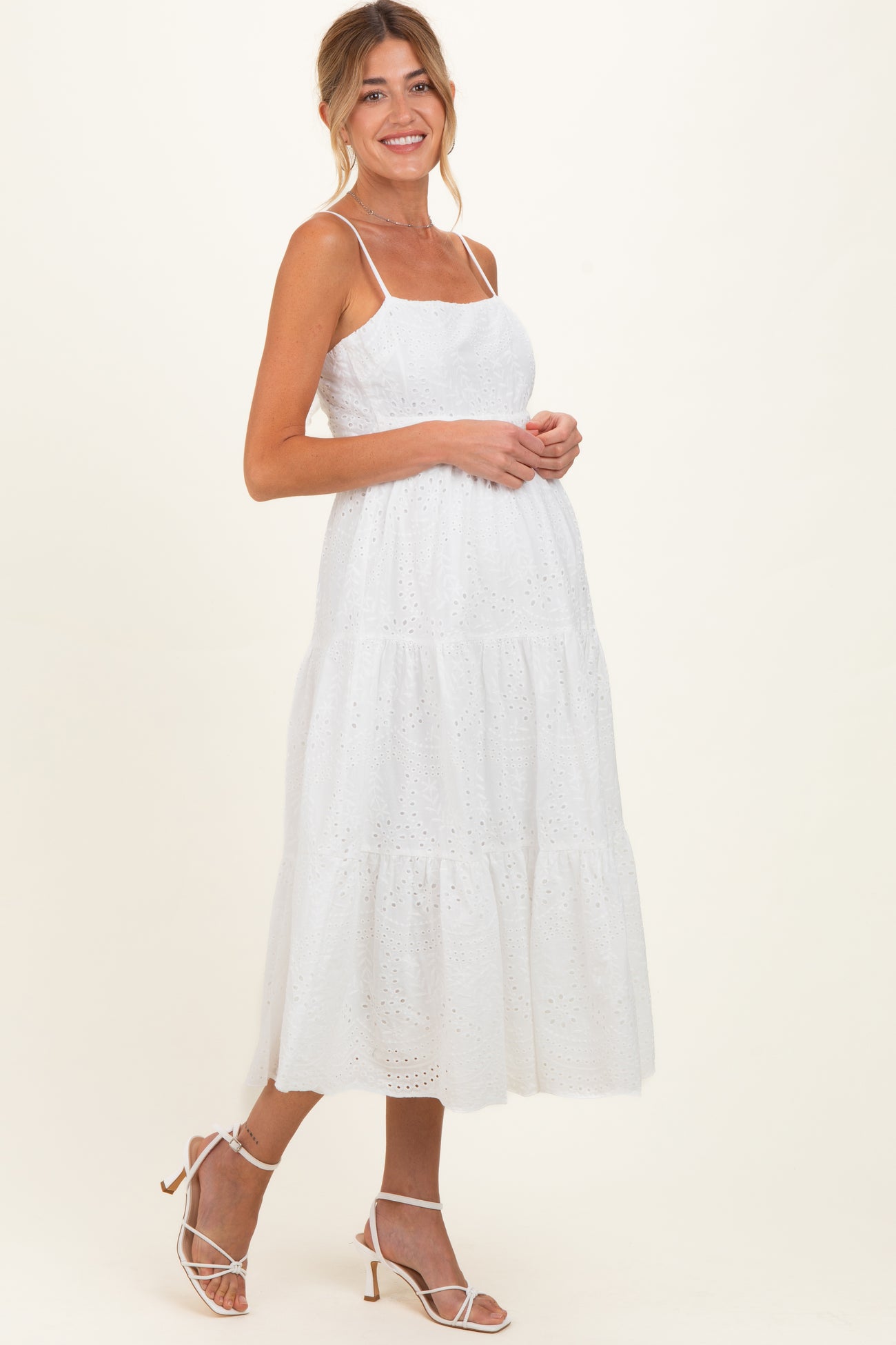 woman wearing a white lace maternity dress with spaghetti straps and a flowing tiered skirt, showcasing her baby bump