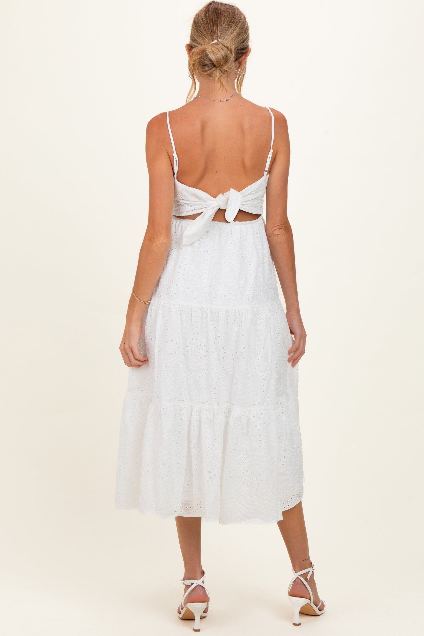 woman wearing a white maternity dress with a tie-back design and tiered skirt, showing her baby bump