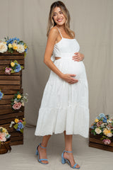 woman wearing a white eyelet maternity dress with cutout details and holding her baby bump