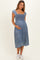 woman wearing a denim maternity dress with a smocked bodice and short puff sleeves, holding her baby bump