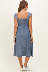 woman wearing a blue denim maternity dress with a smocked bodice and short puff sleeves, shown from the back