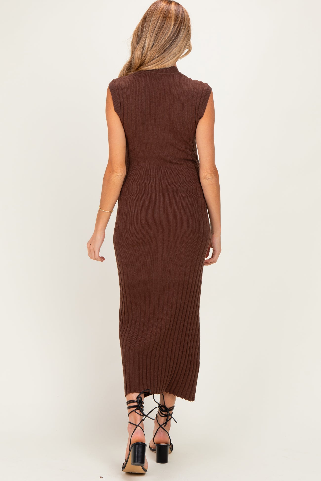woman wearing a brown ribbed maternity midi dress with sleeveless design, standing with her back to the camera