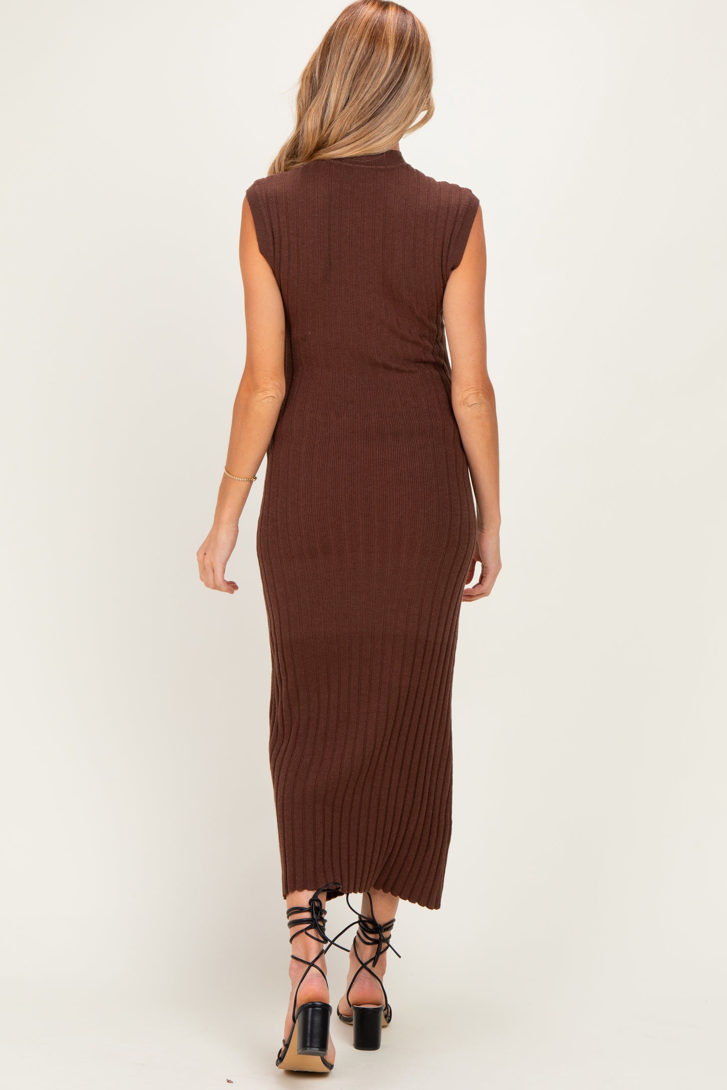 woman wearing a brown ribbed maternity midi dress with sleeveless design, standing with her back to the camera