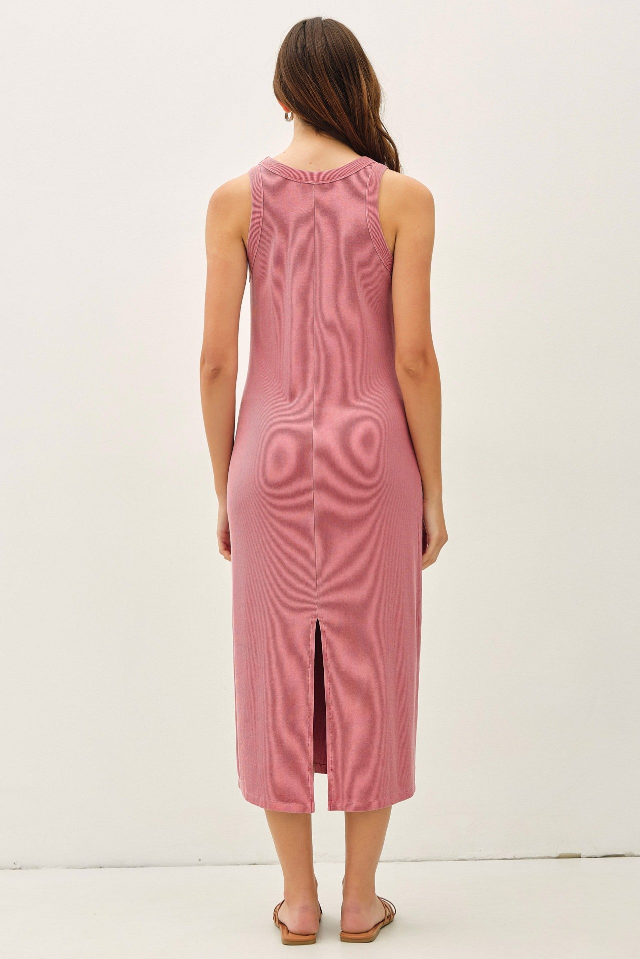 woman wearing a dusty rose sleeveless midi dress with a back slit standing against a plain background