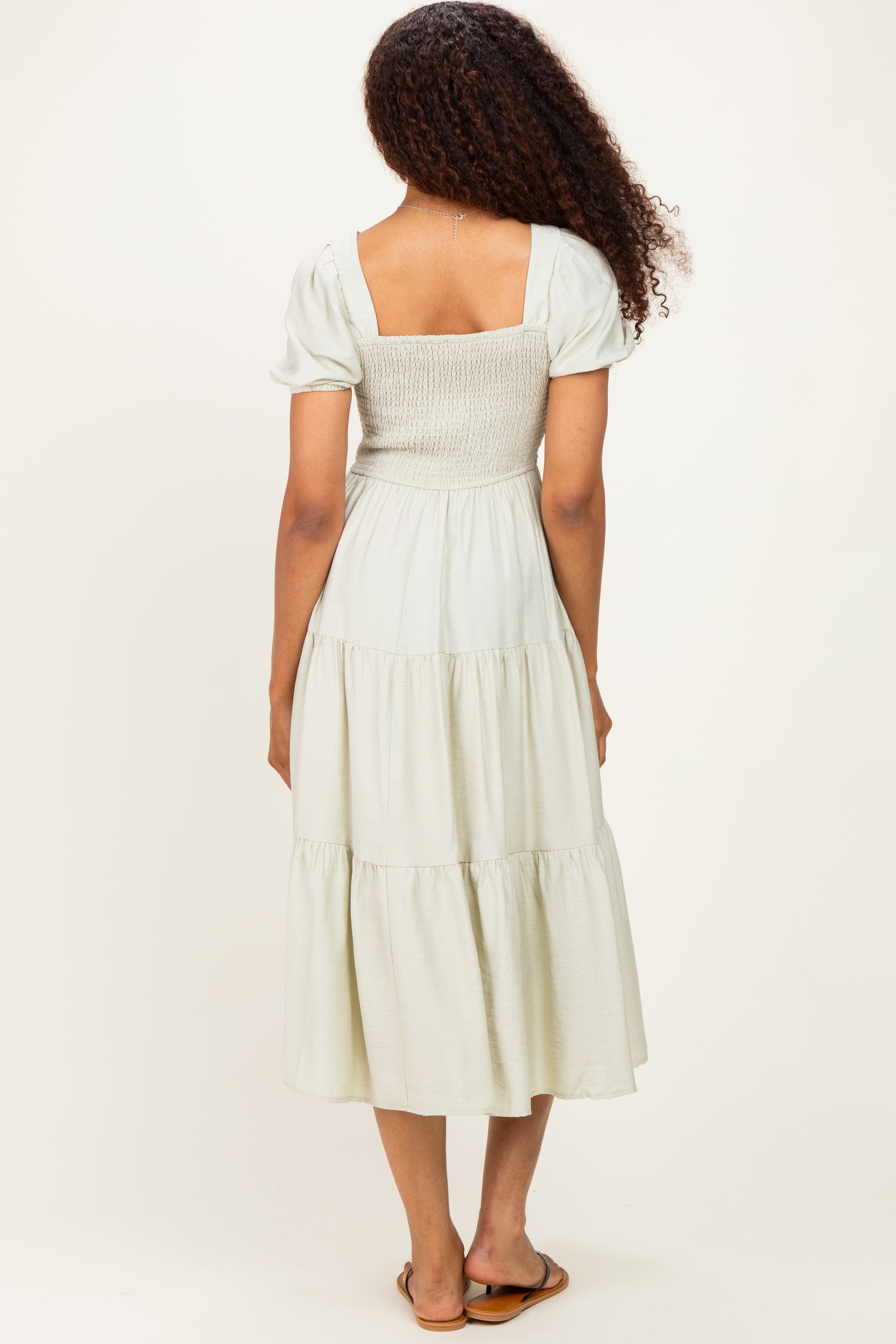 woman wearing a light green tiered maxi dress with a smocked bodice and short puff sleeves, seen from the back