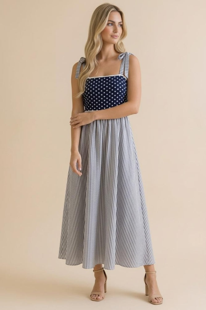 woman wearing a navy and white polka dot and striped maxi dress with ruffled straps and a fitted bodice
