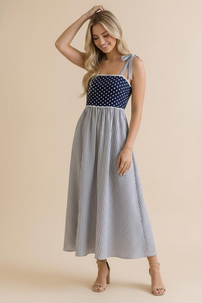 woman wearing a navy and white polka dot and striped maxi dress with tie shoulder straps and a flared skirt