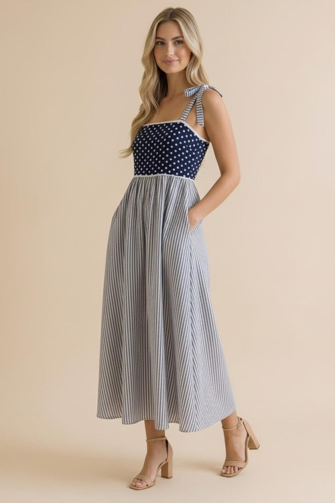 woman wearing a navy polka dot and striped midi dress with ties on the straps and side pockets