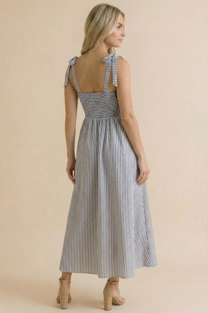 woman wearing a back view of a blue and white striped sundress with tie shoulder straps and a smocked waist