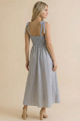 woman wearing a back view of a blue and white striped sundress with tie shoulder straps and a smocked waist