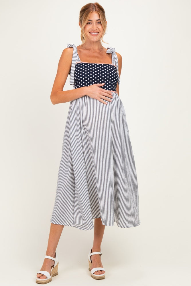 woman wearing a striped maternity dress with a polka dot bodice and bow straps, holding her baby bump