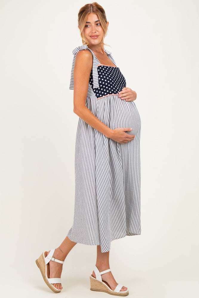 woman wearing a navy and white striped maternity dress with polka dot details and holding her baby bump