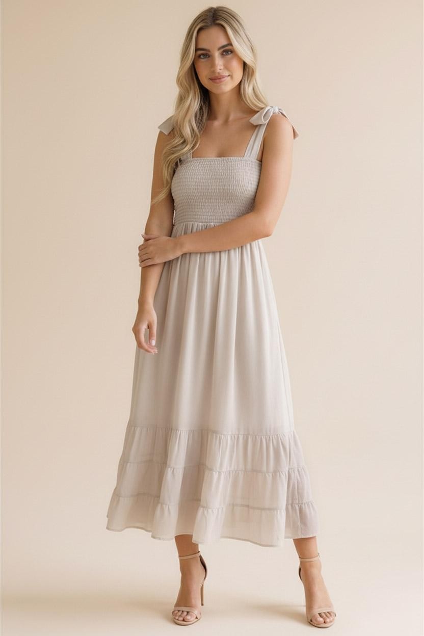 woman wearing a light beige smocked midi dress with ruffled hem and tie shoulder straps