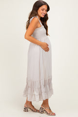 woman wearing a light gray maternity maxi dress with a smocked bodice and ruffled hem, holding her baby bump