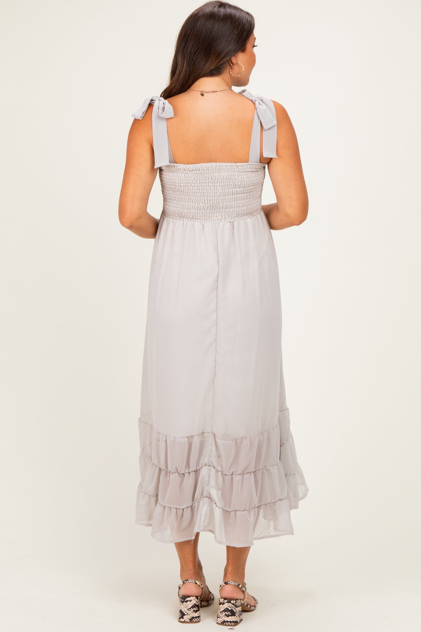 woman wearing a light grey maternity dress with smocked bodice and ruffled hem, shown from the back