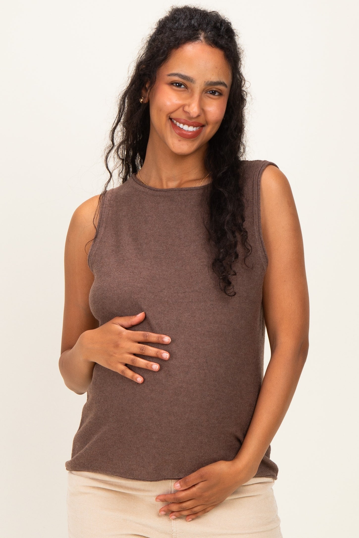 woman wearing a brown sleeveless maternity top and holding her baby bump