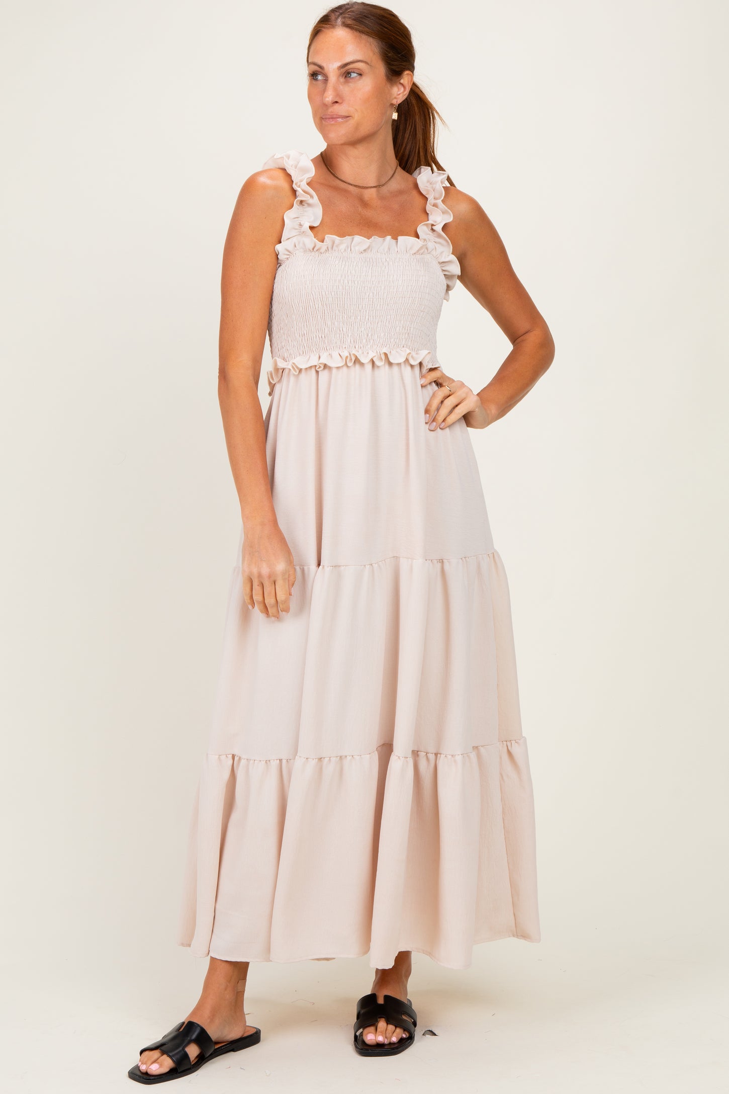 woman wearing a light beige maxi dress with ruffle straps and a smocked top, standing against a plain background