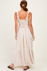 woman wearing a long beige maxi dress with ruffled straps and a smocked bodice, standing with her back to the camera