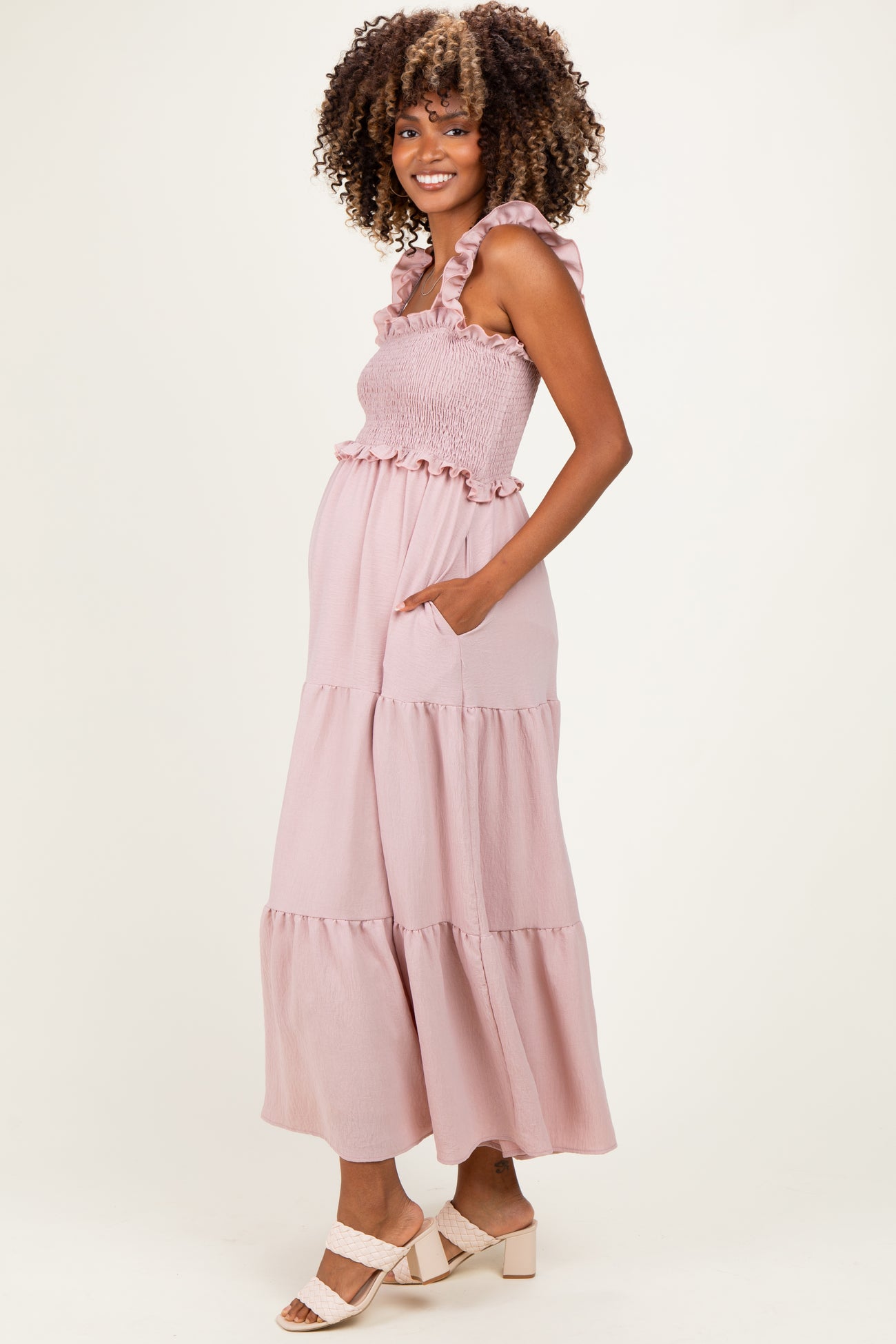 woman wearing a pink ruffled maternity maxi dress with pockets and a smocked bodice, displaying her baby bump