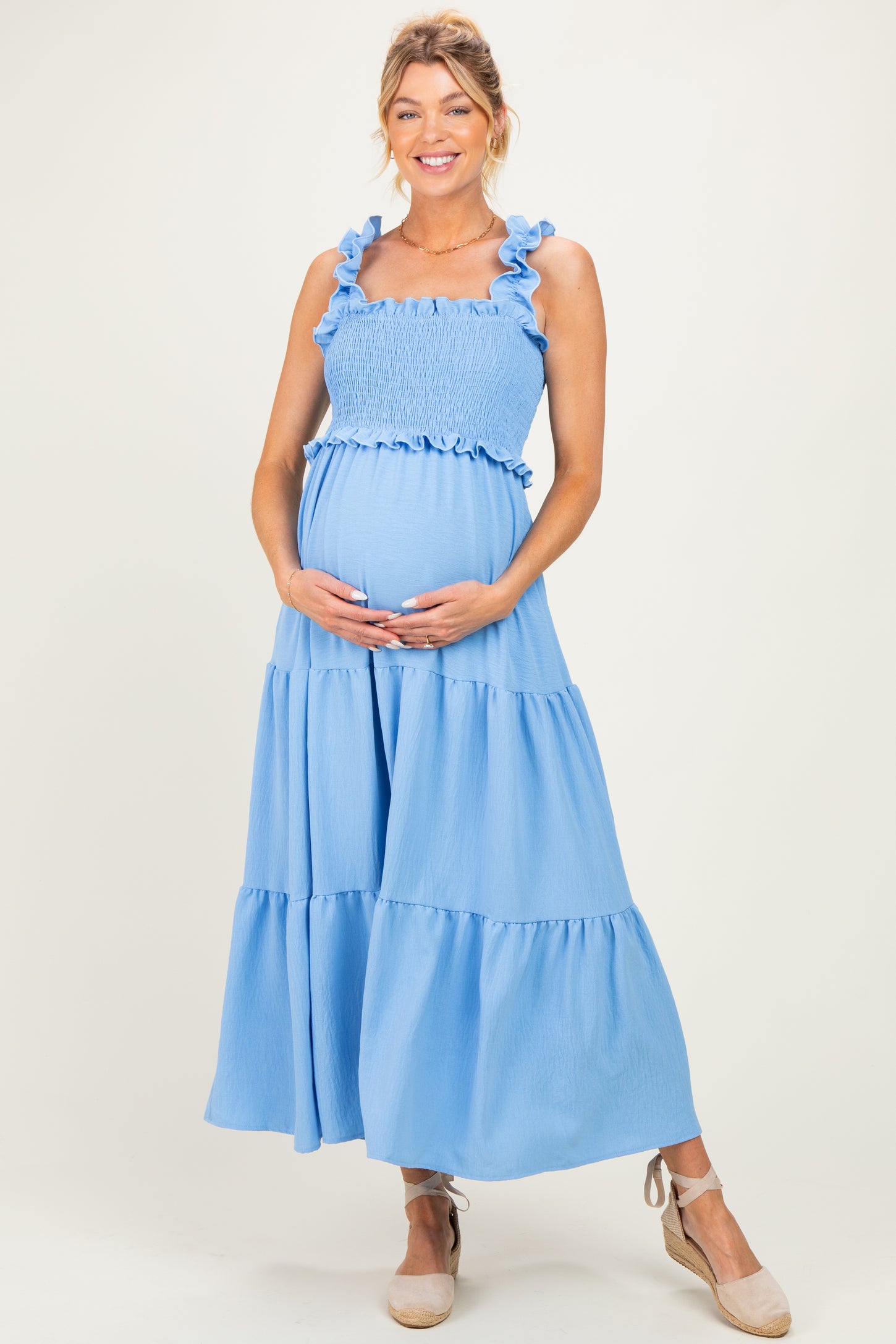 woman wearing a light blue maternity maxi dress with ruffle straps and tiered skirt, holding her baby bump