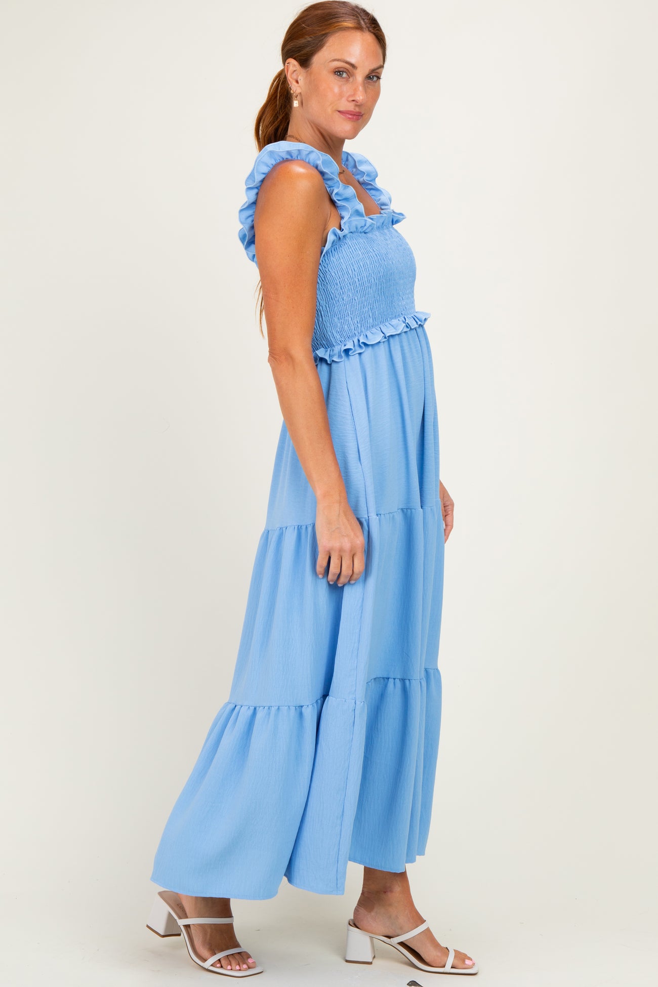 woman wearing a light blue maxi dress with smocked bodice and ruffled straps, standing in profile