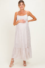 woman wearing a light pink maternity dress with eyelet details, holding her baby bump, featuring a tiered skirt and spaghetti straps
