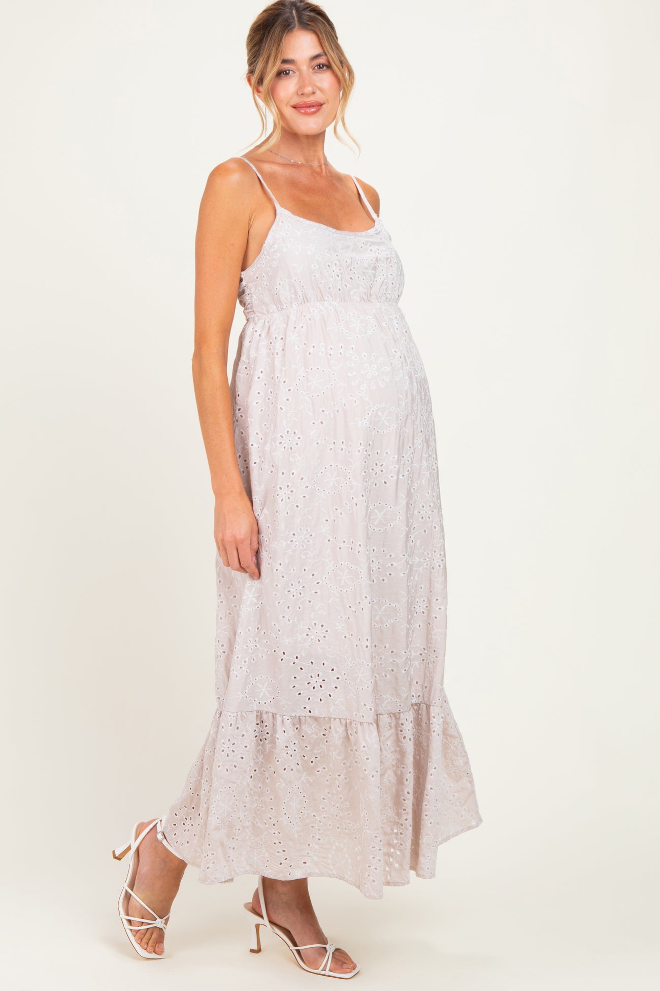 woman wearing a light pink maternity dress with spaghetti straps and eyelet details, showcasing her baby bump