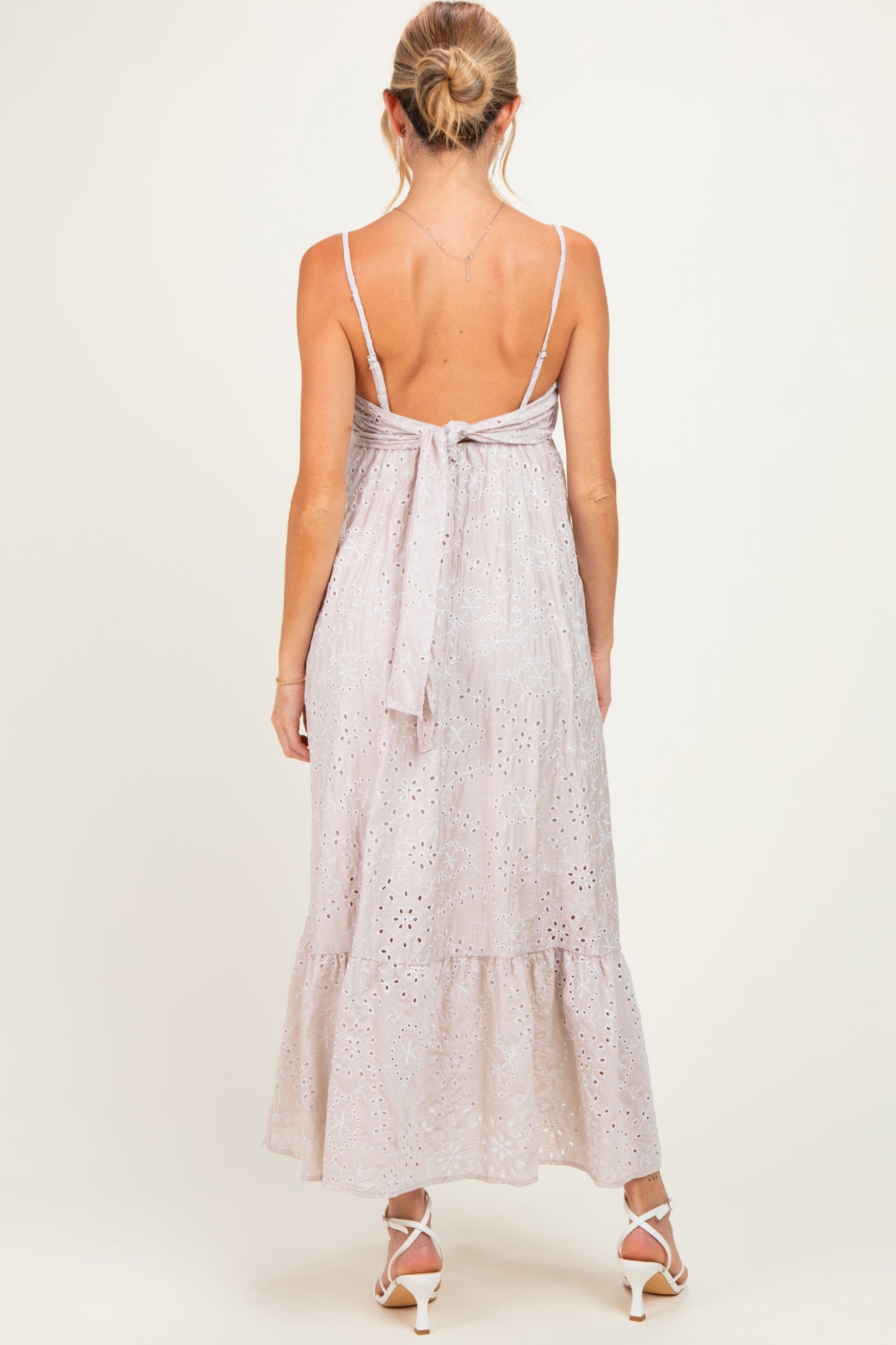 woman wearing a light pink maternity maxi dress with a back tie detail and a tiered skirt