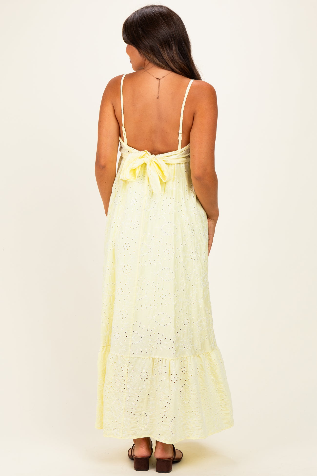 woman wearing a yellow maternity maxi dress with a tie back and eyelet pattern, showing a baby bump