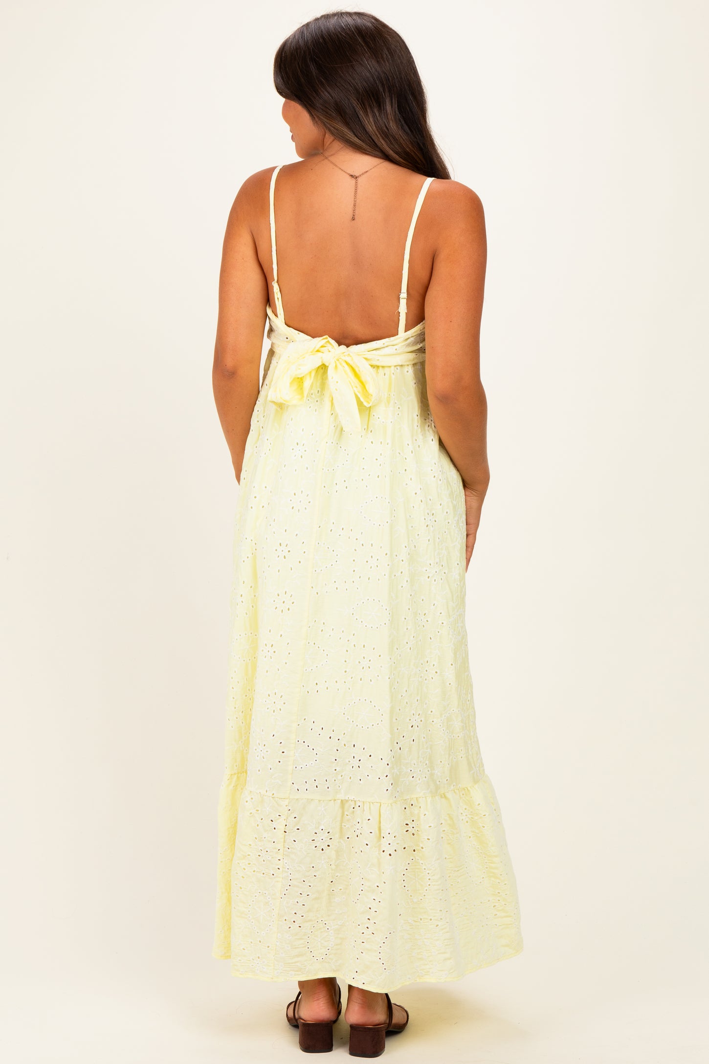 woman wearing a yellow maternity maxi dress with a tie back and eyelet pattern, showing a baby bump