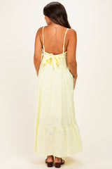 woman wearing a yellow maternity maxi dress with a tie back and eyelet pattern, showing a baby bump