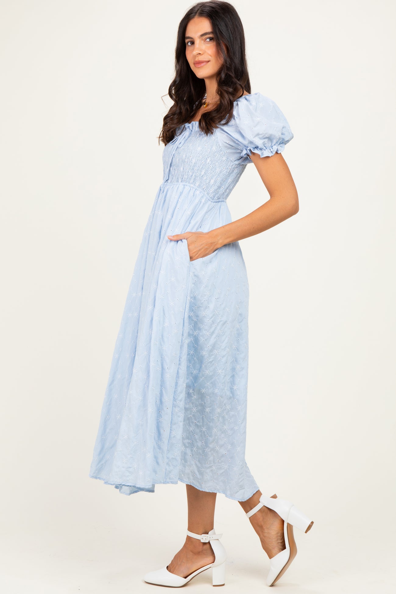 woman wearing a light blue puff sleeve midi dress with pockets and a cinched bodice, styled with white block-heeled shoes