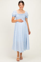 woman wearing a light blue maternity dress with puff sleeves and smocked bodice, gently holding her baby bump