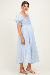 woman wearing a light blue short sleeve smocked maternity dress with a fitted bodice and flowy skirt, baby bump visible